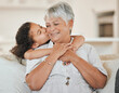 © peopleimages.com - Love, grandmother and grandchild with kiss on sofa with hugging, weekend visit and bonding in home. Happy family, senior woman and girl kid with embrace on couch in living room with support and care