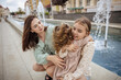 © Татьяна Добрикова - mom and daughters have fun near the fountain on a summer city walk