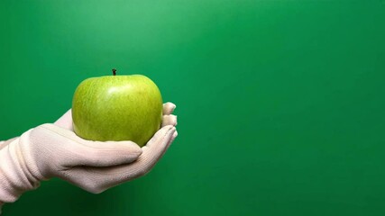 Wall Mural - Video of a person holding an apple on green background