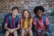 © Ace64 Studio - Three multiethnic children laughing and sitting on the steps of their school, one child is white with short blonde hair wearing blue shorts