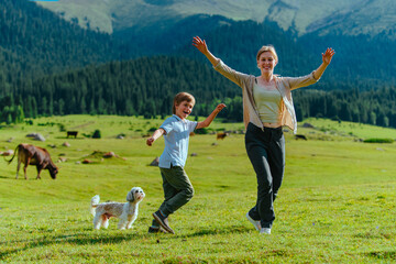 Wall Mural - Happy young woman with her son and dog running on mountains meadow