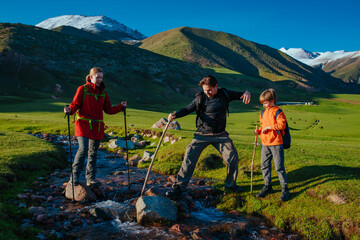 Sticker - Parents hiking with their son across mountains stream on summer day