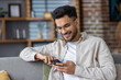 © Tetiana - Smiling man using smartphone while relaxing on couch at home, enjoying digital content and staying connected