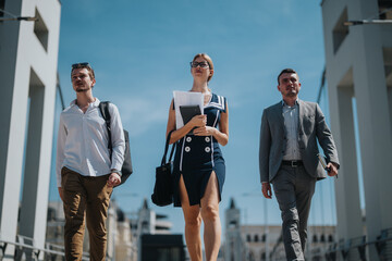 Three confident business professionals walk on a bridge, symbolizing teamwork and determination. They wear modern business attire, emphasizing a dynamic urban work environment under a clear sky.