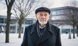 © Miklos - An older man in a black coat and cap looks directly at the camera in front of a white building
