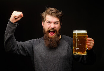 Wall Mural - Happy bearded man with beer mug celebrating victory with raised hand. Excited man drinking draft delicious beer. Winner expression. Handsome male with mug beer making winning gesture with raised arm.