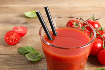 Tasty tomato juice in glass, basil leaves and fresh vegetables on wooden table, closeup