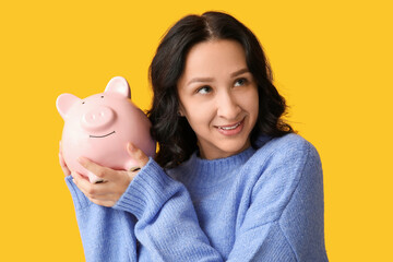 Wall Mural - Pretty young woman with piggy bank on yellow background