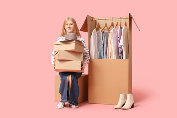 Wall Mural - Beautiful young happy woman and wardrobe boxes with clothes on pink background