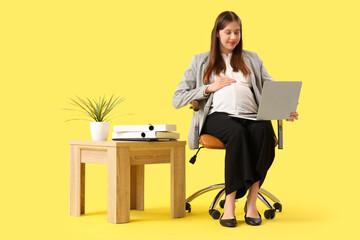 Canvas Print - Young pregnant businesswoman with laptop in chair on yellow background