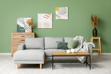 Sticker - Interior of stylish living room with grey sofa, coffee table and pictures on green wall