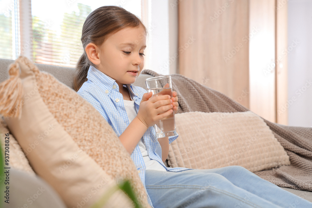 Cute little girl drinking water on sofa at home