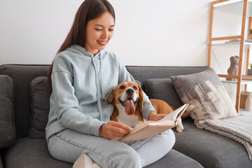 Sticker - Young woman reading book and sitting with adorable Beagle dog on sofa in living room