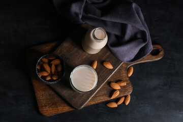 Wall Mural - Glass and bottle of fresh almond milk with nuts on black background