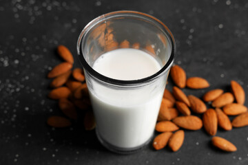 Glass of fresh almond milk and nuts on black background