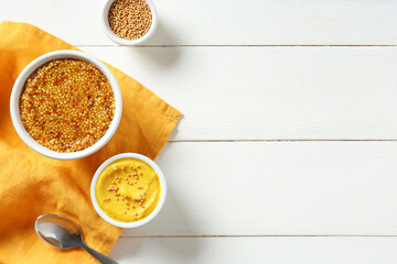 Wall Mural - Bowls with Dijon mustard and seeds on white wooden background