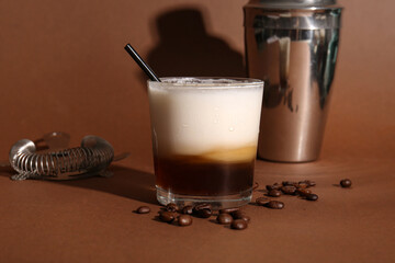 Wall Mural - Glass of White Russian cocktail with coffee beans and shaker on brown background