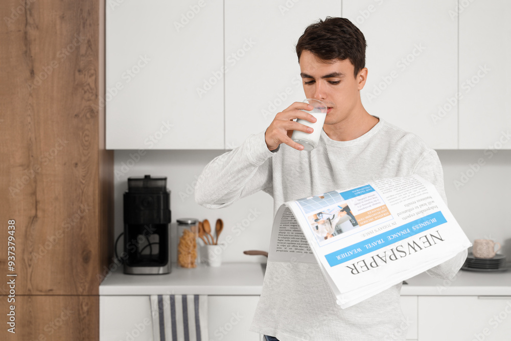Young man with newspaper drinking milk in kitchen