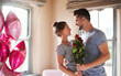 © Chanelle2000/peopleimages.com - Flowers, couple and affection in bedroom for love, connection and bonding together with surprise. Home, man and woman with balloon for relationship, commitment and anniversary celebration in house