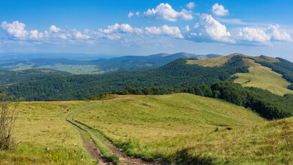 Green summer mountain landscape with beautiful cloudy sky. Two tourists with backpacks walking along a dirt road