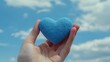 © JH45 - Hand Holding a Blue Heart Against a Cloudy Sky