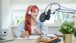 © wattana - Cheerful young woman recording a podcast in a bright and modern studio.