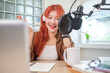 © wattana - Attractive young woman wearing headphones and speaks into a professional microphone,  recording a podcast in modern studio.