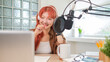 © wattana - Attractive young woman wearing headphones and speaks into a professional microphone,  recording a podcast in modern studio.