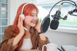 © wattana - Attractive young woman wearing headphones and speaks into a professional microphone,  recording a podcast in modern studio.