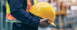 © alexandre - close-up image of a construction worker dressed in safety gear, holding a yellow hard hat securely