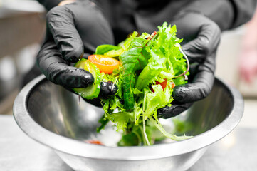 Sticker - Close-up of hands in black gloves preparing a fresh salad with mixed greens and cherry tomatoes in a stainless steel bowl, highlighting the concept of hygiene and healthy eating