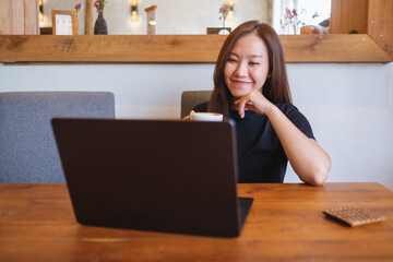 Canvas Print - Portrait image of a young woman drinking coffee while working on laptop computer at home