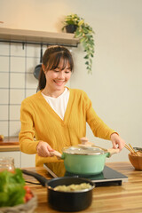 Pretty young woman in a light yellow cardigan is enjoying cooking in the kitchen at home