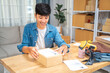 © kudosstudio - Happy young online seller man putting the shipping label on the box before shipping it to his online customer