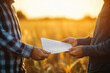 © alisluch - Farmers exchanging documents in a field at sunset, discussing agricultural business, rural contract agreement, handshake deal