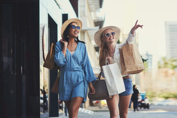 Pointing, friends and happy women with shopping bags in city for fashion sunglasses, discount or luxury clothes. Black Friday, girls or gift outdoor at mall for retail, street promotion or sales deal