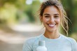 © Kanakorn - Smiling woman holding a water bottle, post-run, outdoor setting, satisfied with fitness progress
