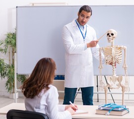 Wall Mural - Young male teacher doctor, skeleton and female student in the cl