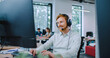 © ihorvsn - View from behind of two large monitors of Caucasian male sitting at desk Smiling while talking with customer. Man working hard in big office. Wear on wired headset with attached microphone.