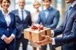 © thanakrit - Businessman Giving A Gift To Colleagues In An Office Setting.