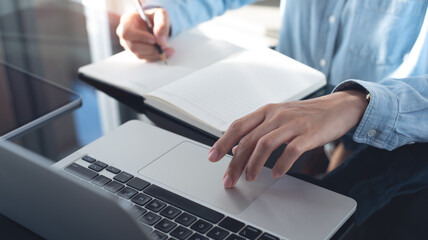 Wall Mural - Business woman working on laptop computer and writing note on notebook. Female student searching the information on laptop computer during online studying, e-learning,  business planning