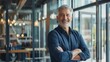 © JINGWEN - Smiling handsome businessman with crossed arms in modern office, middle-aged gray-haired man exuding confidence, business success concept.