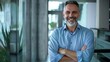 © JINGWEN - Smiling handsome businessman with crossed arms in modern office, middle-aged gray-haired man exuding confidence, business success concept.