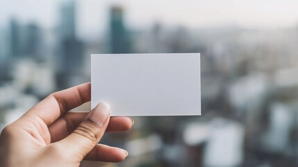 Close-up of a blank white business card mockup being handed by a person with neat fingernails, against a softly blurred urban cityscape