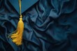 © volga - Elegant graduation cap with gold tassel on blue fabric background