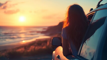 Woman leaning out of car window admiring a sunset over the ocean.