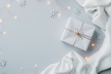 a white wrapped gift sits on a light gray background surrounded by white fabric, twinkle lights, and