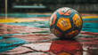 © Sawyer0 - Kolorowa, zużyta piłka znajduje się na mokrym, wielokolorowym boisku, przywołując poczucie nostalgii i trwałego uroku sportów.