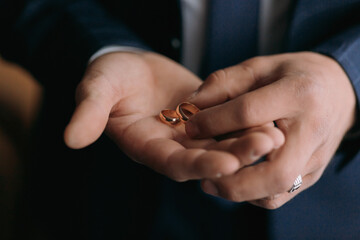 A man is holding two gold wedding rings in his hand