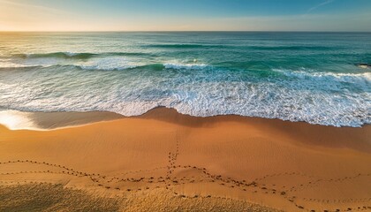 Wall Mural - Top View of Tranquil Beach With Footprints Leading to Serene Ocean Waves